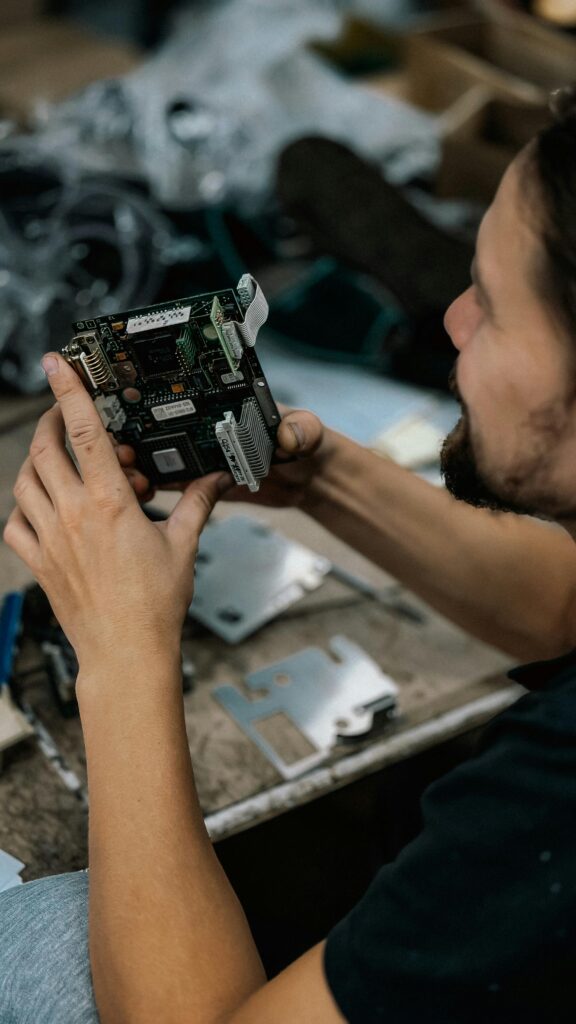 pexels-photo-34054502-34054502 Focused technician examining a circuit board with precision in a cluttered workshop environment.